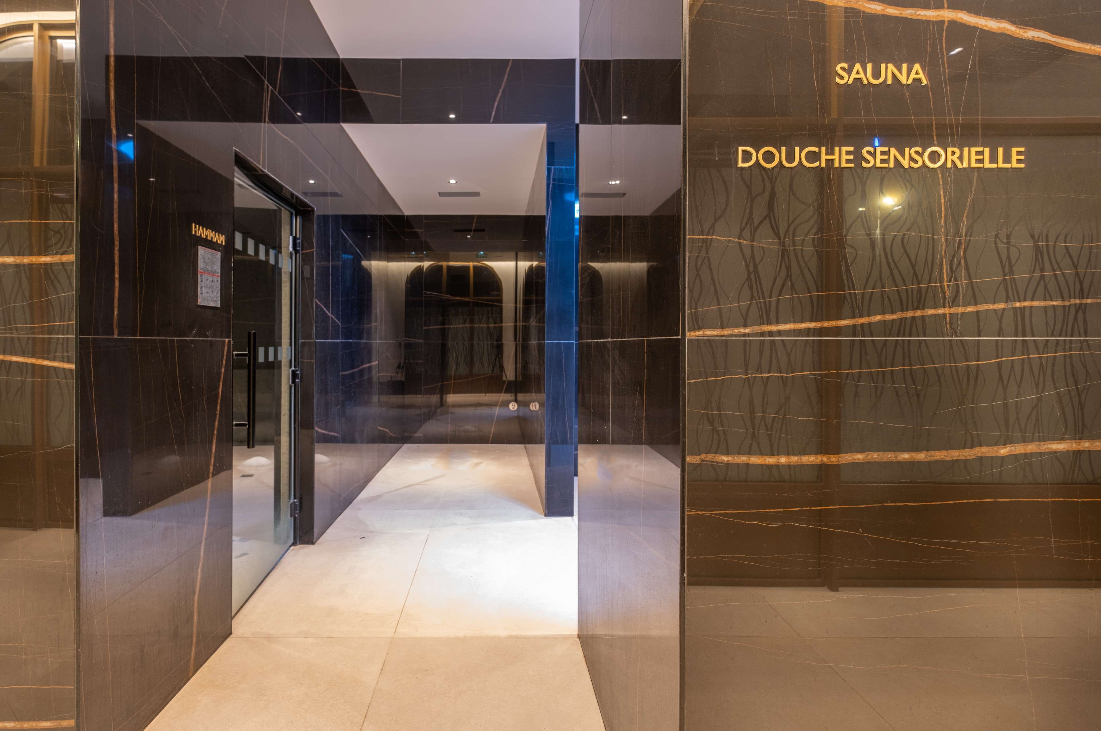 Un interior moderno con una puerta de cristal que da a un espacio con la indicación "SAUNA" y "DOUCHE SENSORIELLE".