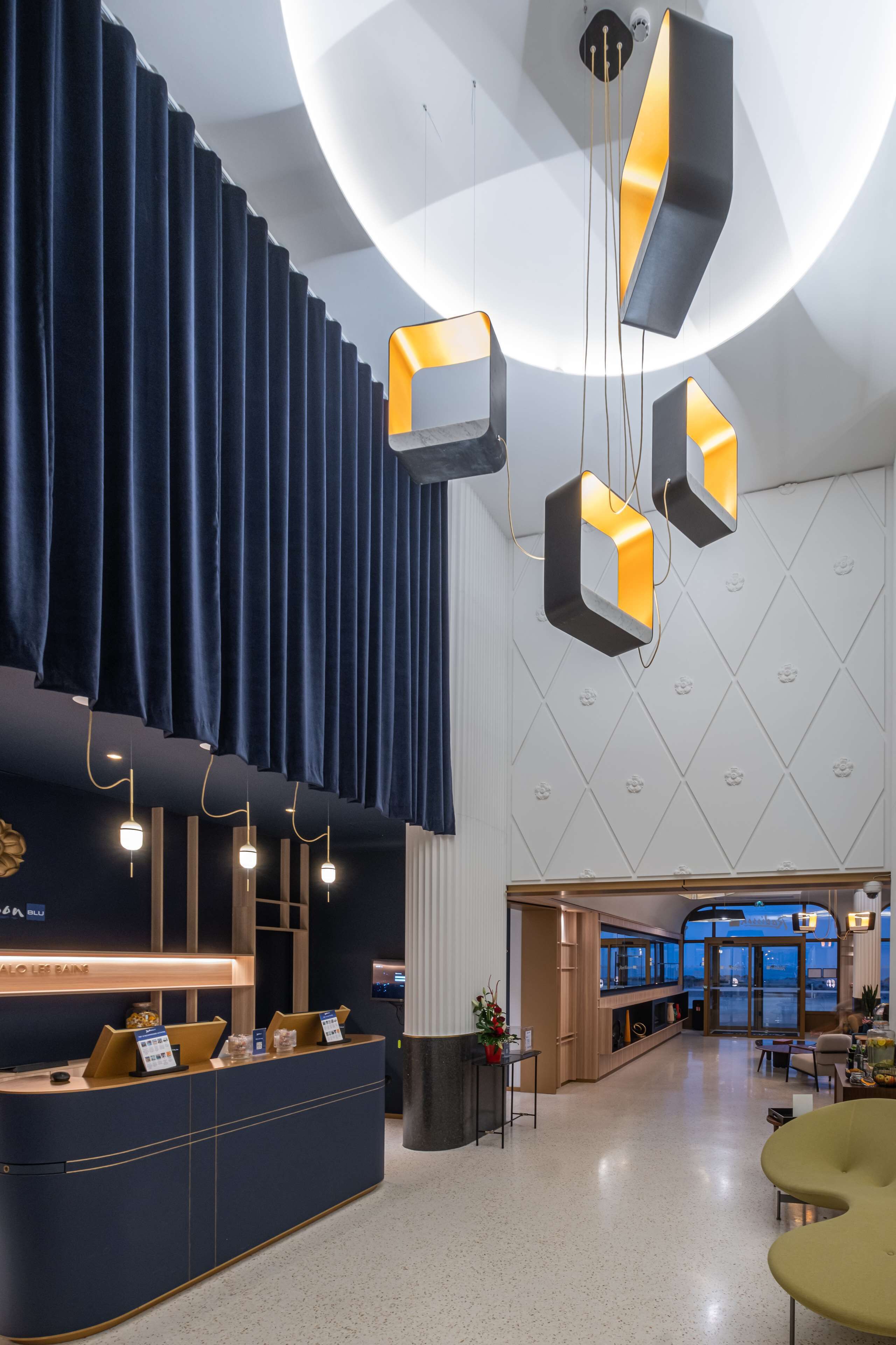 A modern hotel lobby with a reception desk, a large window offering a view, and a seating area with a yellow chair.