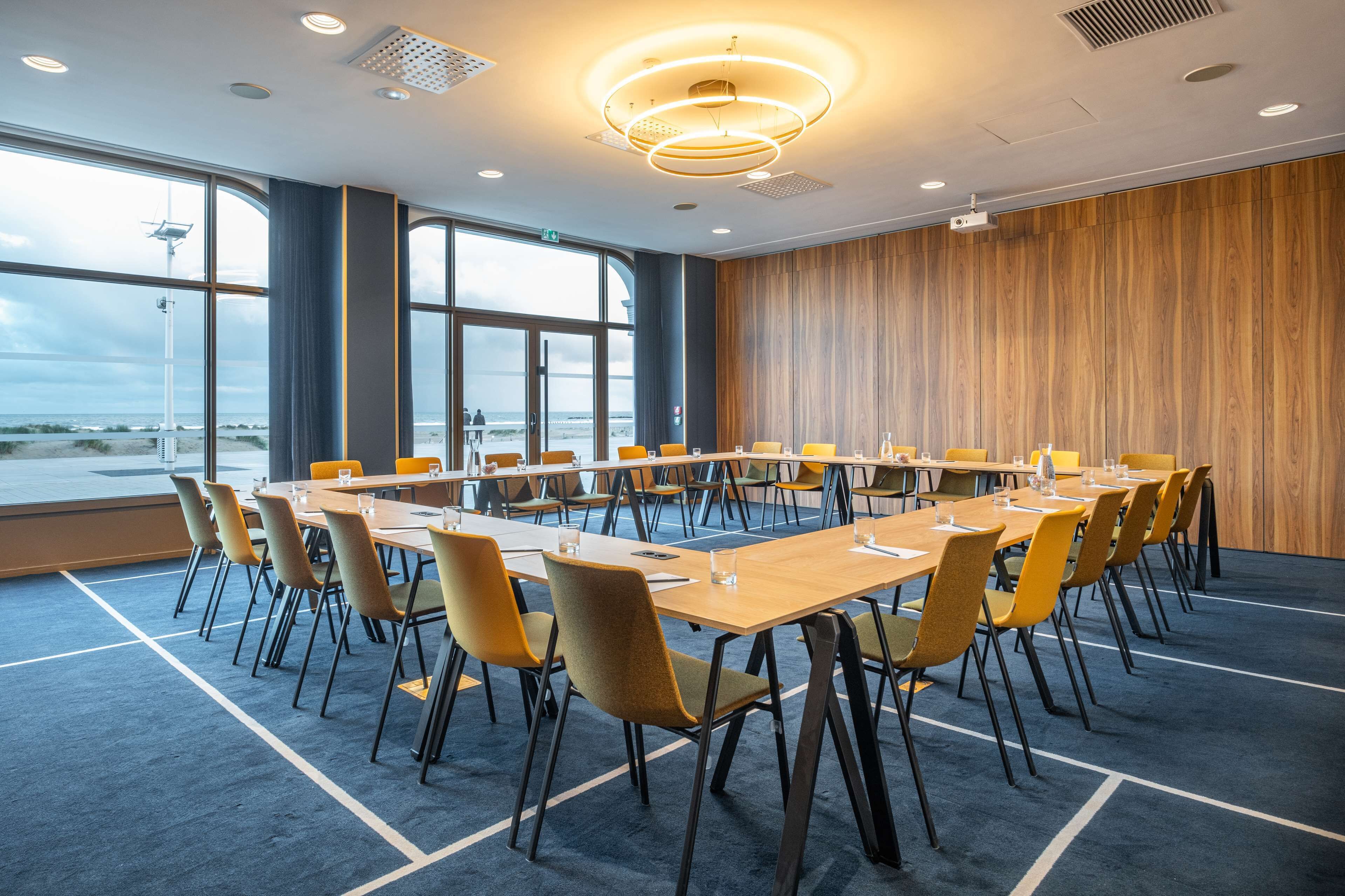 A conference room with a large table, chairs, and a view of the beach through large windows.