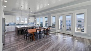 Una cocina amplia con una isla central, ventanas grandes y un comedor con mesa y sillas de madera.