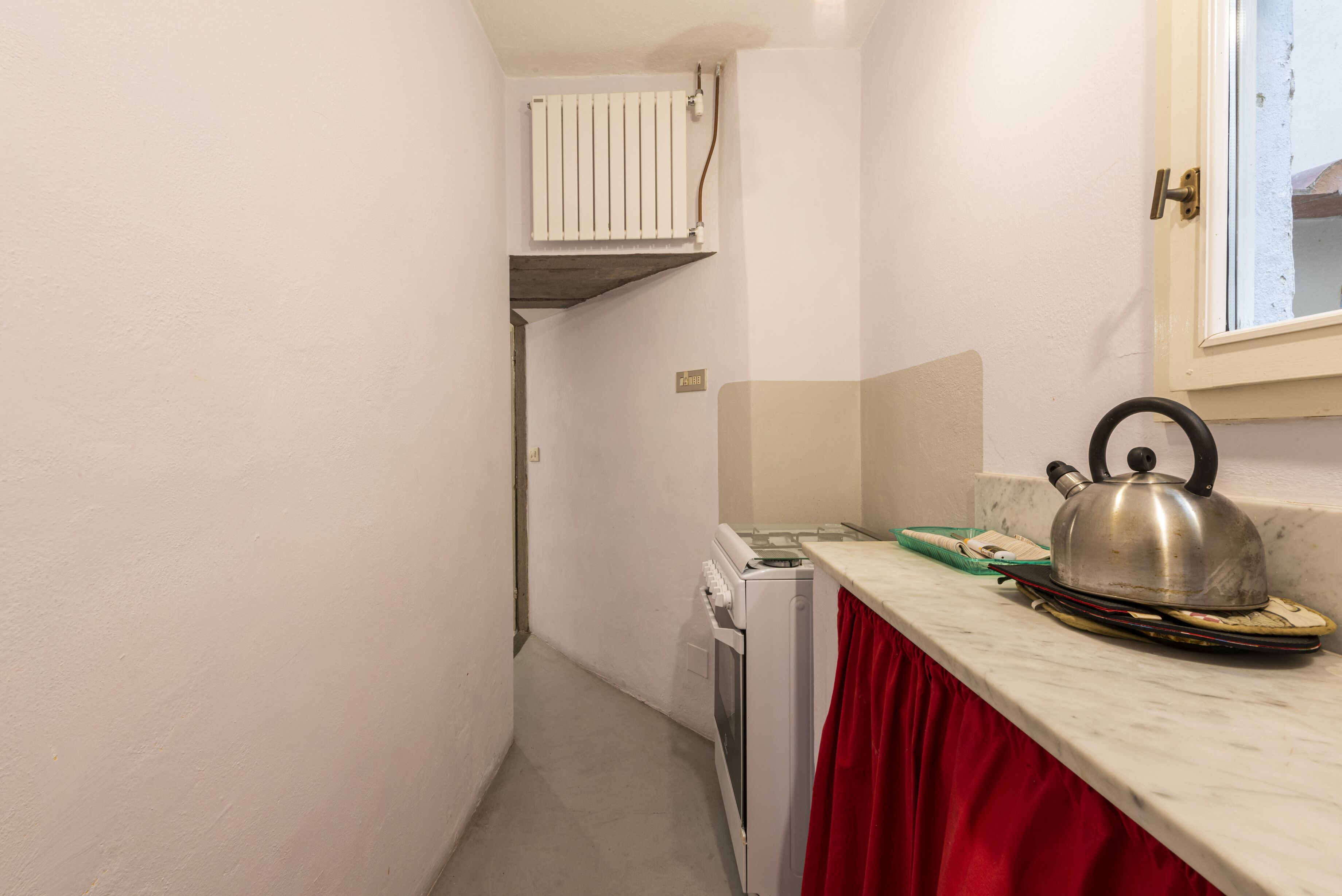 A narrow kitchen with a white refrigerator, a white oven, and a red curtain.