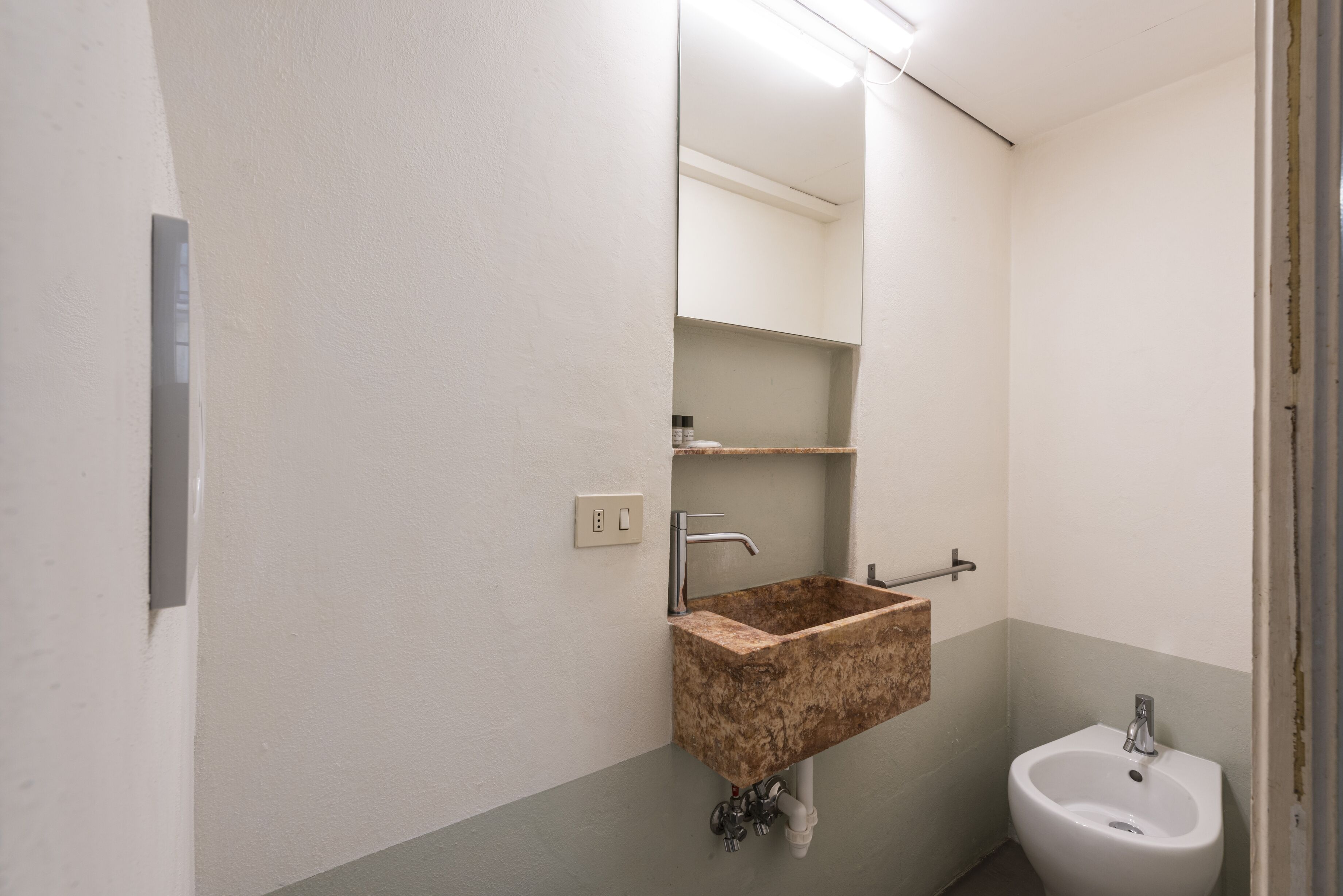 A bathroom with a marble sink, a mirror, a white pedestal sink, and a towel rack.