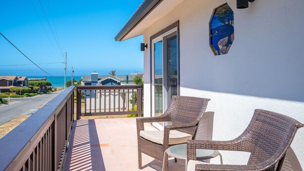 Un balcon avec des fauteuils en osier et une porte vitrée, donnant sur une zone côtière.