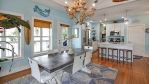 A modern kitchen with white cabinets, a central island with bar stools, and a chandelier. - The Nautilus (Tybee Island)