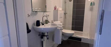 A modern bathroom with a white sink, toilet, and shower.