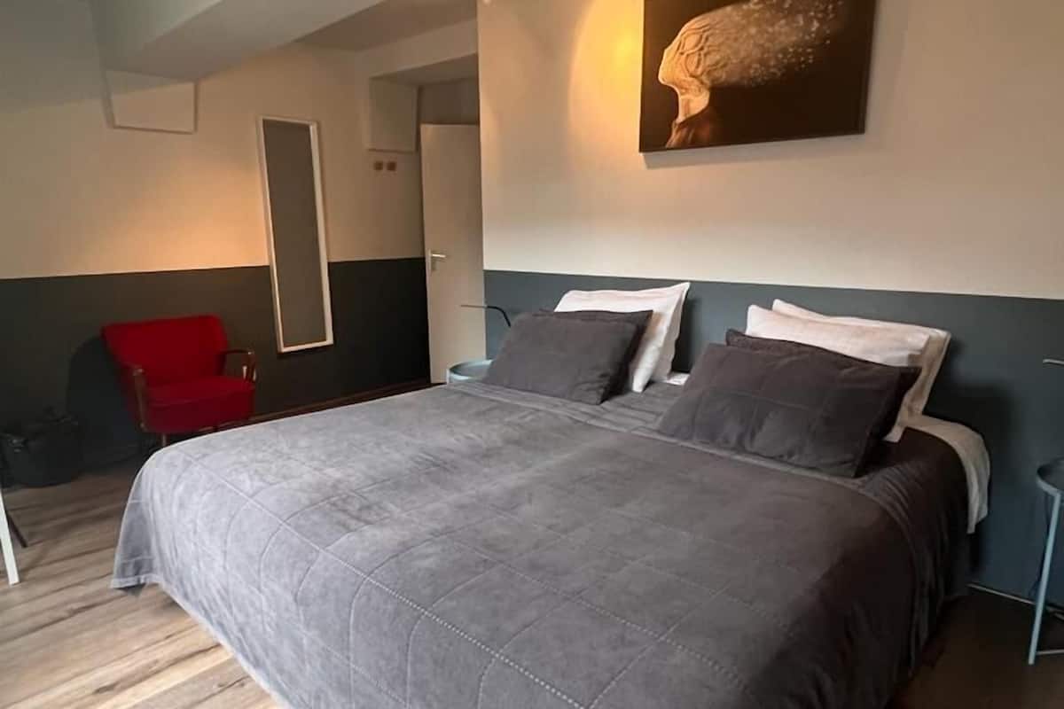 A bedroom with a large bed, a red chair, and a painting on the wall.