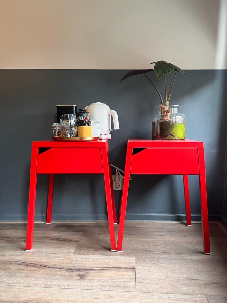 Two red tables with various items on them, including a white kettle and a plant in a glass container.