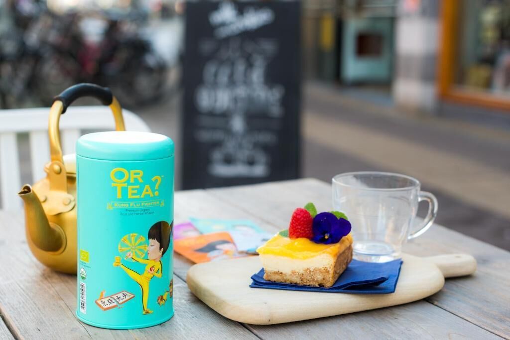 Une table avec une théière, une tasse en verre et une part de gâteau décorée de fruits, le tout posé sur une planche en bois.