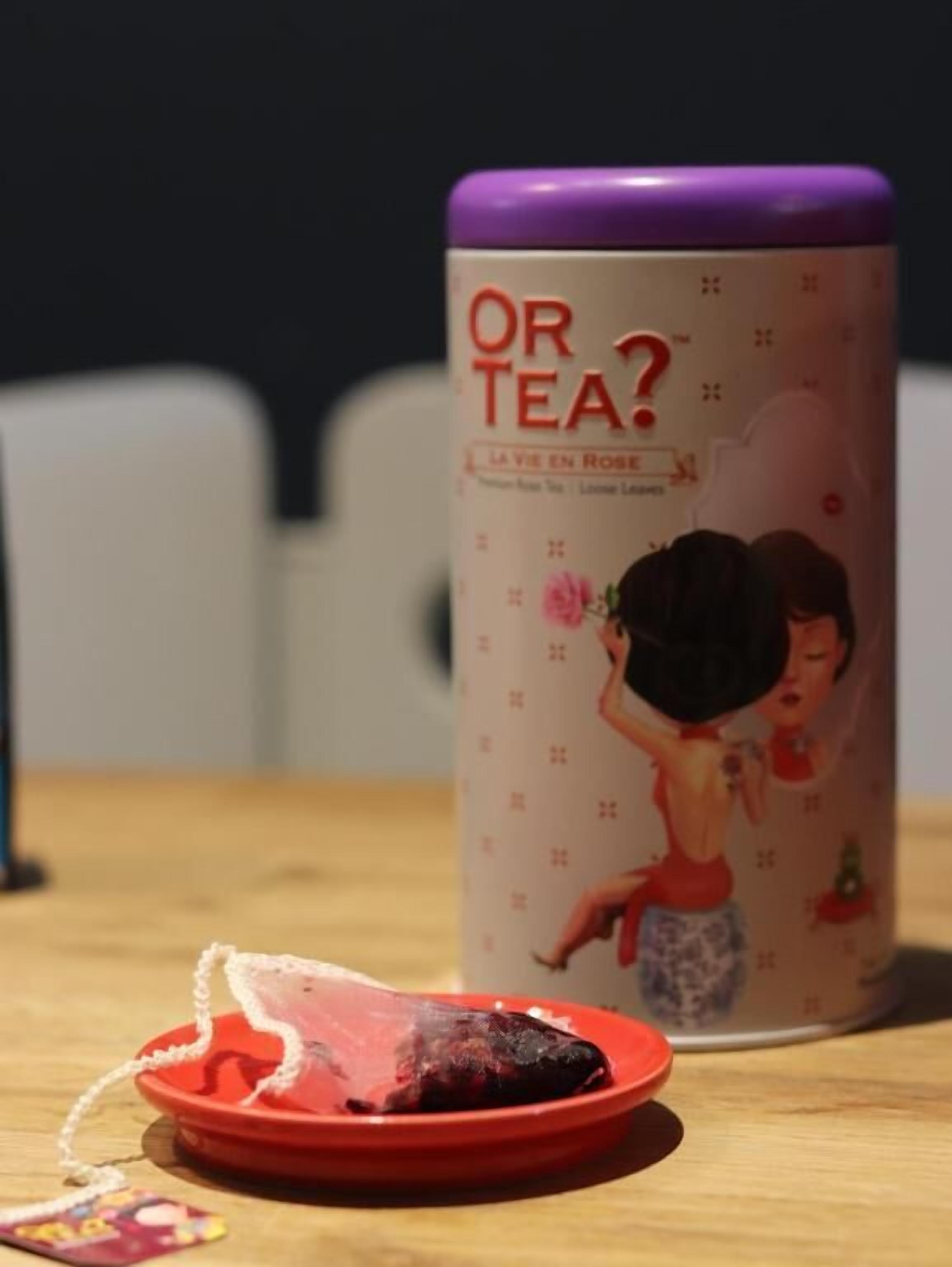 A tea canister with a purple lid and a label that reads "OR TEA?" with a cartoon illustration of a woman and a child.