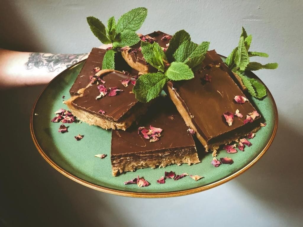 Een bord met chocoladegedekte desserts, versierd met muntblaadjes en rozenblaadjes.