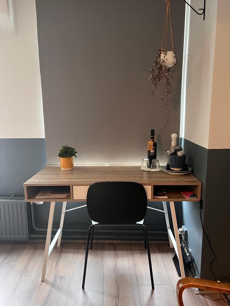 A corner desk with a black chair, a small potted plant, a bottle, and a hanging plant.
