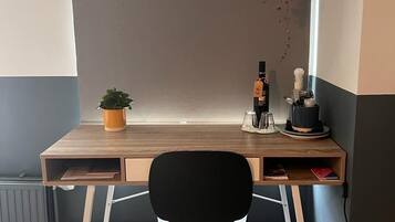 A corner desk with a black chair, a small potted plant, a bottle, and a hanging plant.