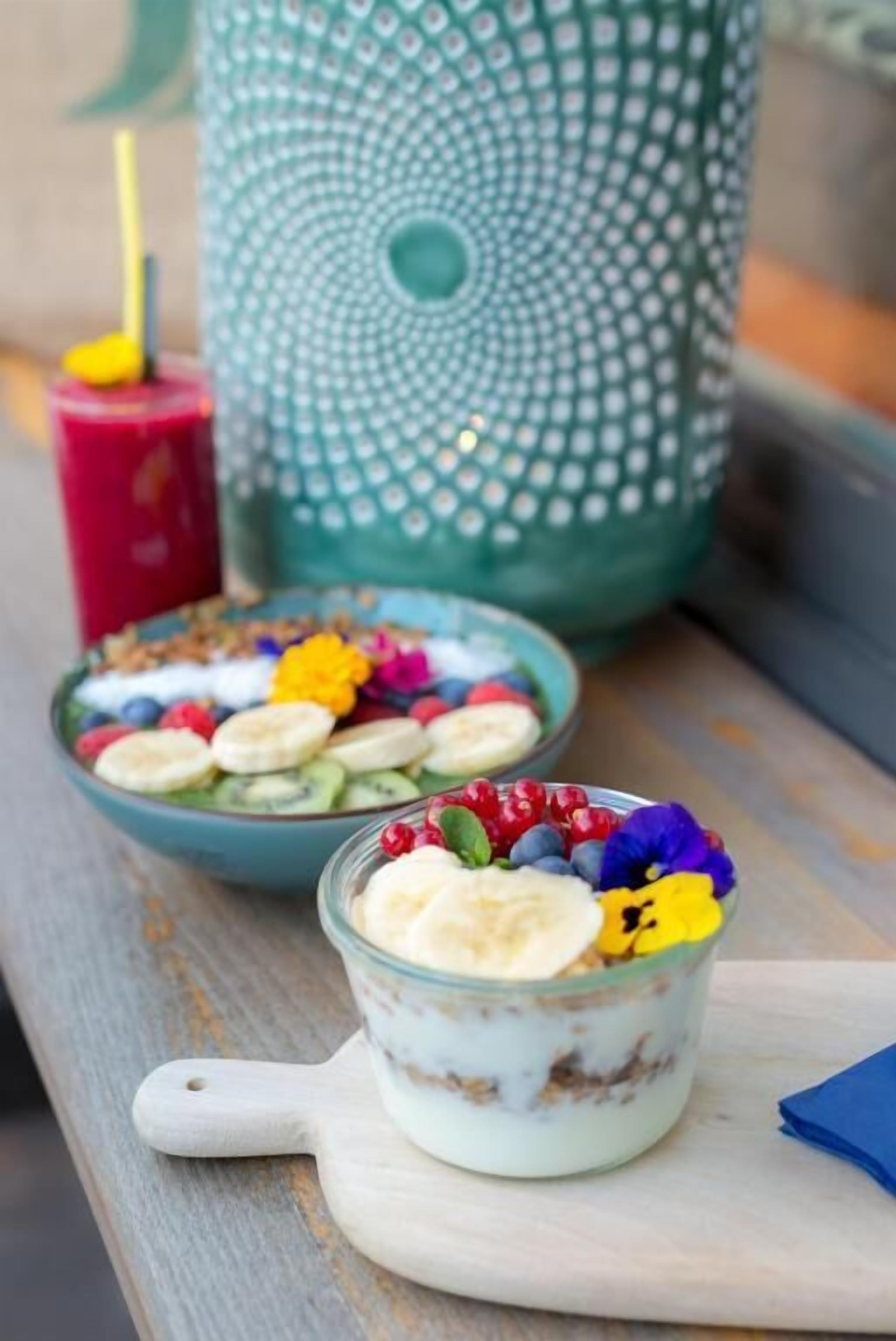 A bowl of yogurt with fruits and granola, a glass of yogurt with fruits, and a decorative candle holder.
