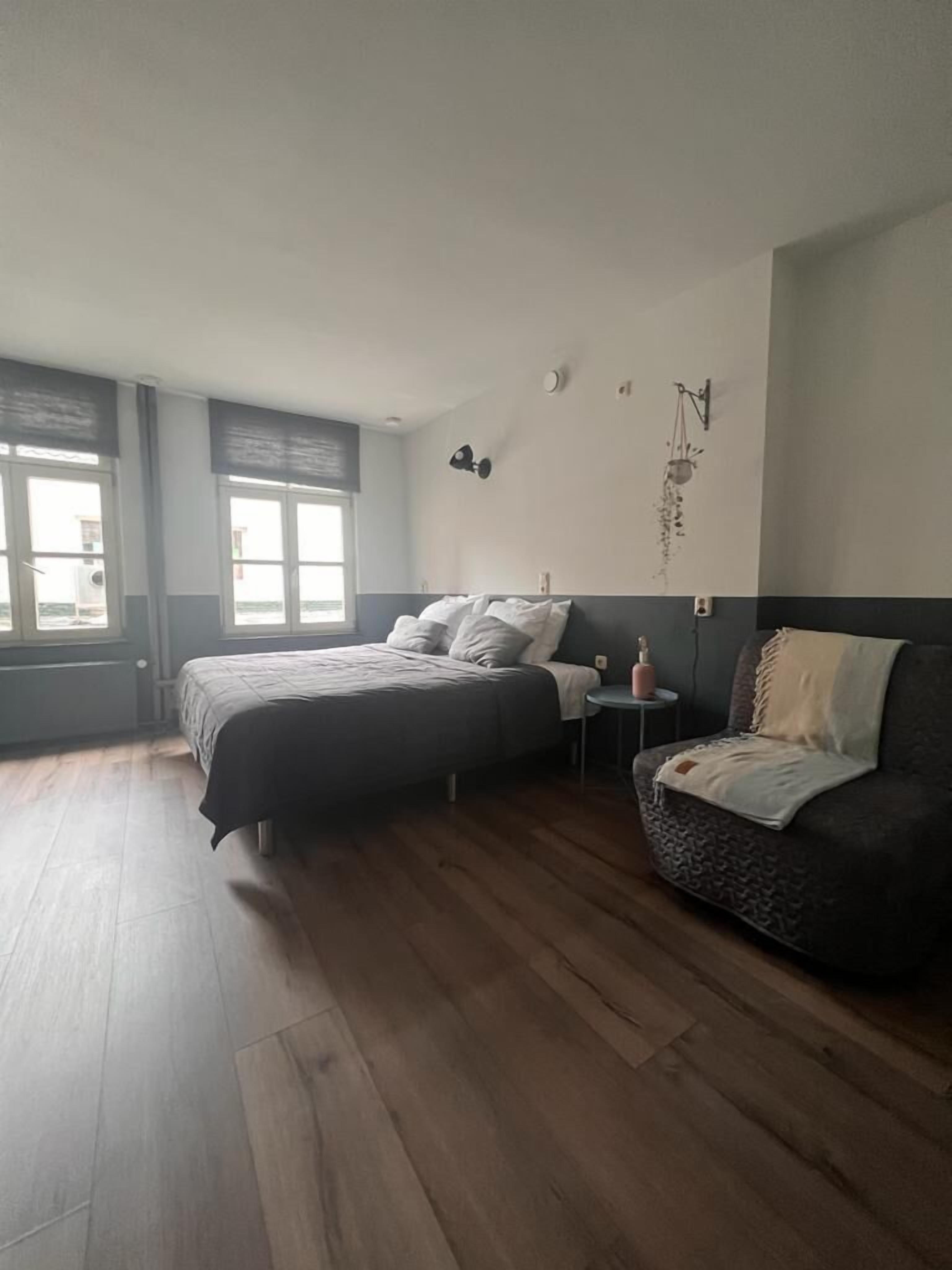 Ein Schlafzimmer mit einem Bett, einem Sofa und einem kleinen Tisch. Es gibt Fenster und eine Wandleuchte.