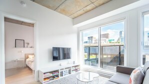 Un salon moderne avec une grande fenêtre, un téléviseur à écran plat, un canapé et une petite table.