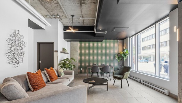 Un espace de bureau moderne avec un canapé gris, une table ronde et une grande fenêtre donnant sur la rue.