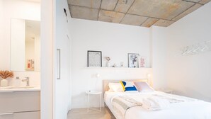 Une chambre moderne avec un grand lit, une table de chevet, une commode et une étagère murale agrémentée d’objets décoratifs.