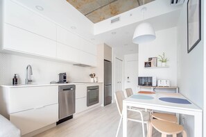 A modern kitchen with white cabinetry, stainless steel appliances, and a dining area with a white table and chairs.