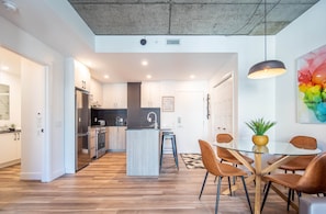 A modern kitchen with a central island, stainless steel appliances, and a dining area with a glass table and brown chairs.