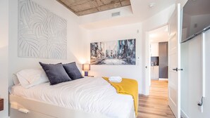 Un dormitorio moderno con cama, obras de arte y vista a la cocina.
