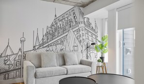 Una sala de estar moderna con un sofá gris, una mesita redonda y un gran mural en la pared de un castillo.