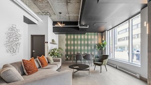 A modern office space with a grey sofa, a round table, and a large window offering a view of the street. - The Caïman Complex, 707 + Parking (Québec City)