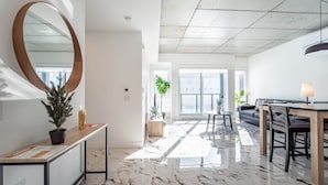 A modern interior with a marble floor, a large wooden-framed mirror, a dining area with a table and chairs, and a sofa. - The Caïman Complex, 707 + Parking (Québec City)