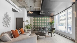 Ein moderner Arbeitsraum mit einem grauen Sofa, einem runden Tisch und einem großen Fenster mit Blick auf die Straße.
