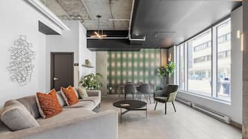 A modern office space with a grey sofa, a round table, and a large window offering a view of the street.