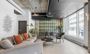 A modern office space with a grey sofa, a round table, and a large window offering a view of the street.