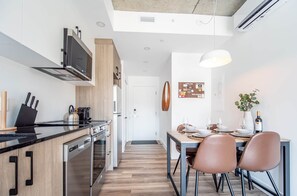 A modern kitchen with a built-in oven, microwave, and stove. There is a dining area with a table set for two, chairs, and a potted plant.