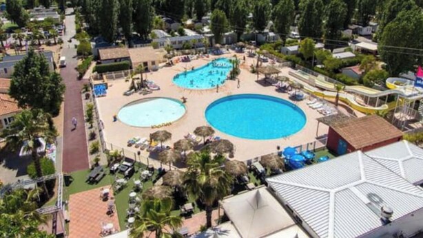 Ett semesterområde med flera pooler, en huvudbyggnad och omgivande grönska.