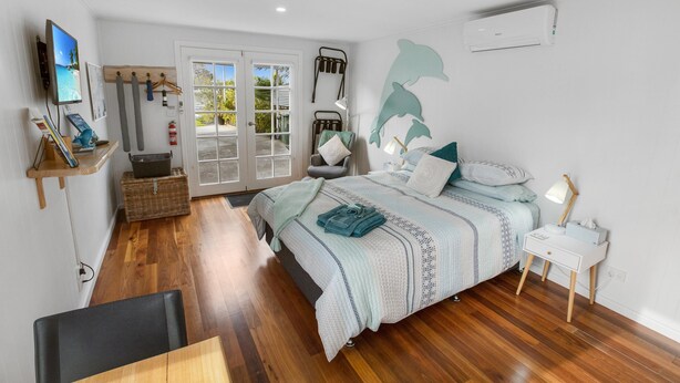 Un dormitorio con cama, mesita de noche y televisor en un estante.