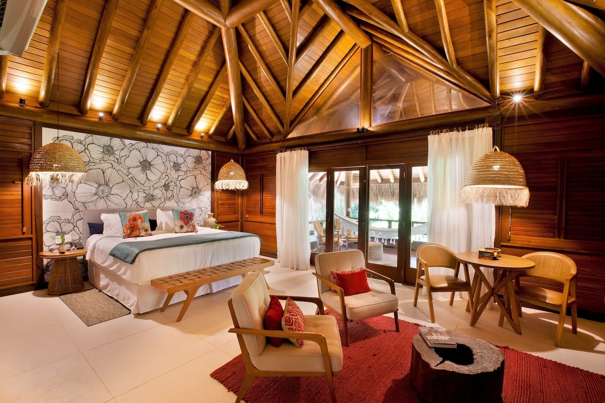 Une chambre spacieuse avec un grand lit, deux fauteuils, une petite table et un plafond en bois.
