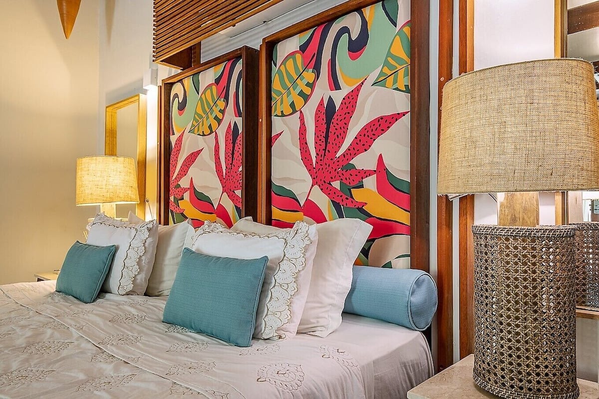 Une chambre d’hôtel avec un lit, des oreillers, une lampe et un mur orné d’un motif abstrait et coloré.