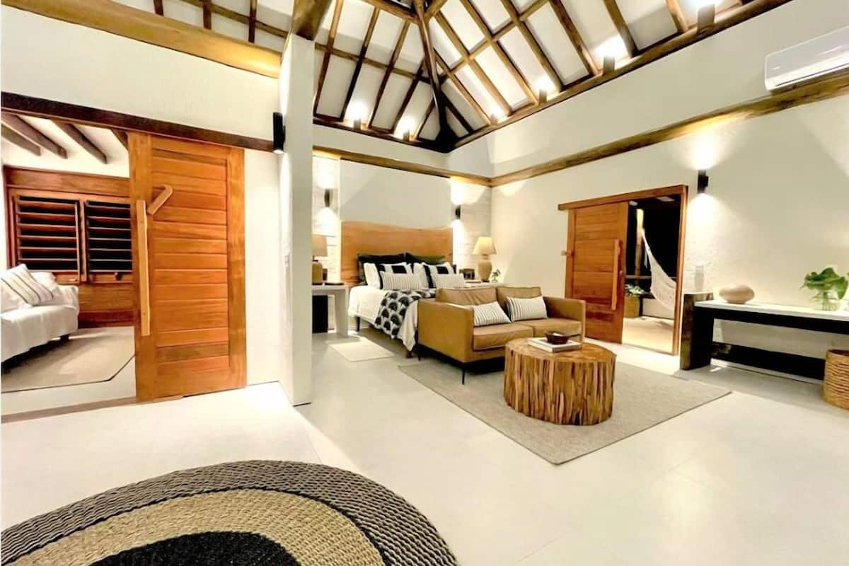 Un vaste espace de vie doté d’un haut plafond, d’un confortable ensemble de canapés, d’une table basse ronde en bois et d’une grande porte en bois.