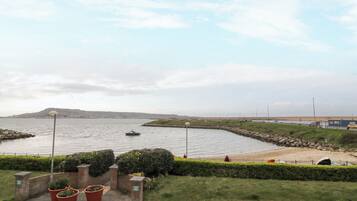 Une vue sur la côte, avec un bateau sur l’eau, une promenade pavée et une zone herbeuse agrémentée de plantes en pot.