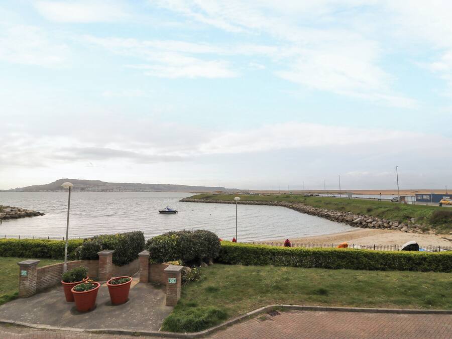 Une vue sur la côte, avec un bateau sur l’eau, une promenade pavée et une zone herbeuse agrémentée de plantes en pot.