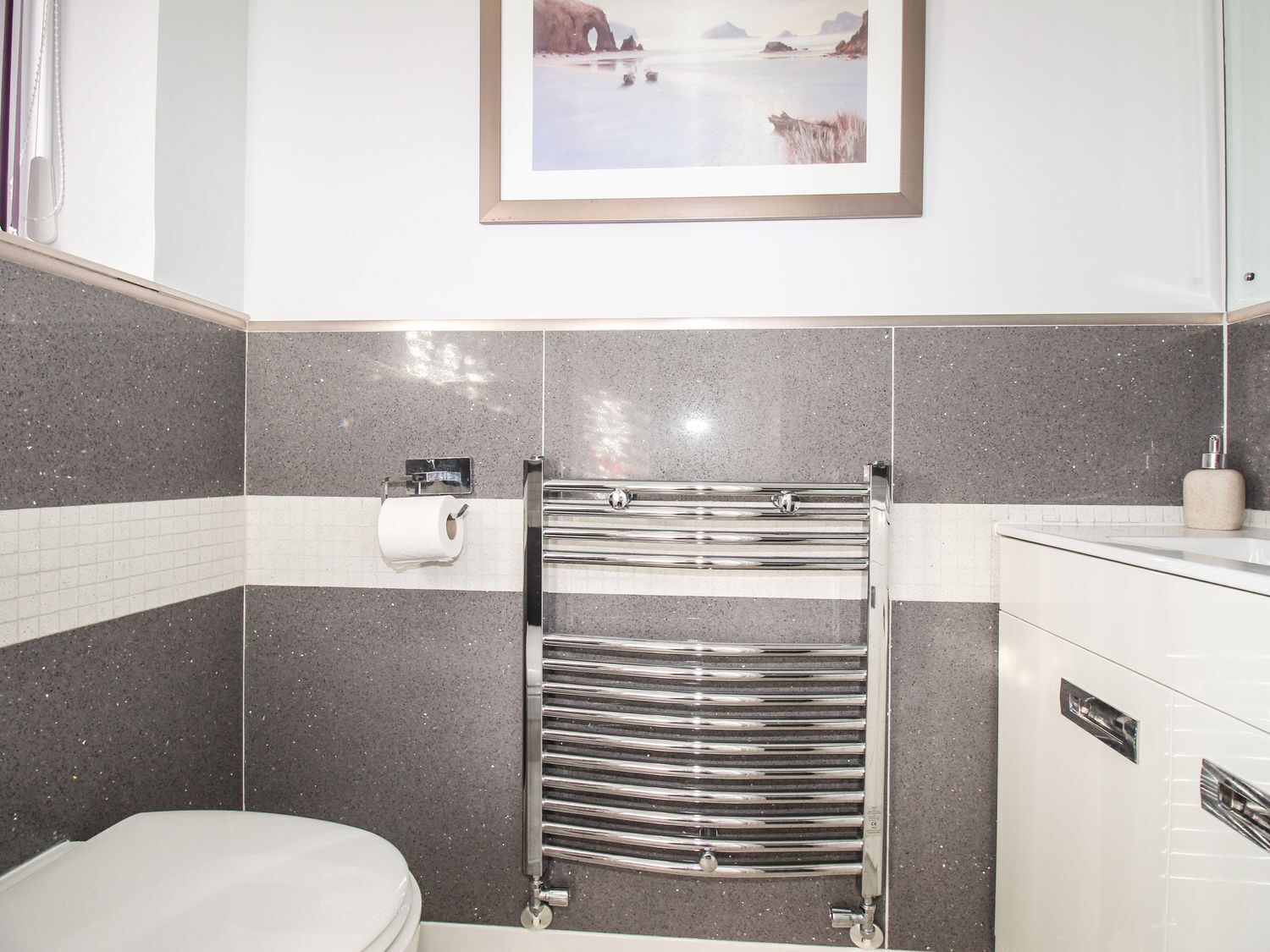 A modern bathroom with a toilet, a towel rack, and a framed picture on the wall.
