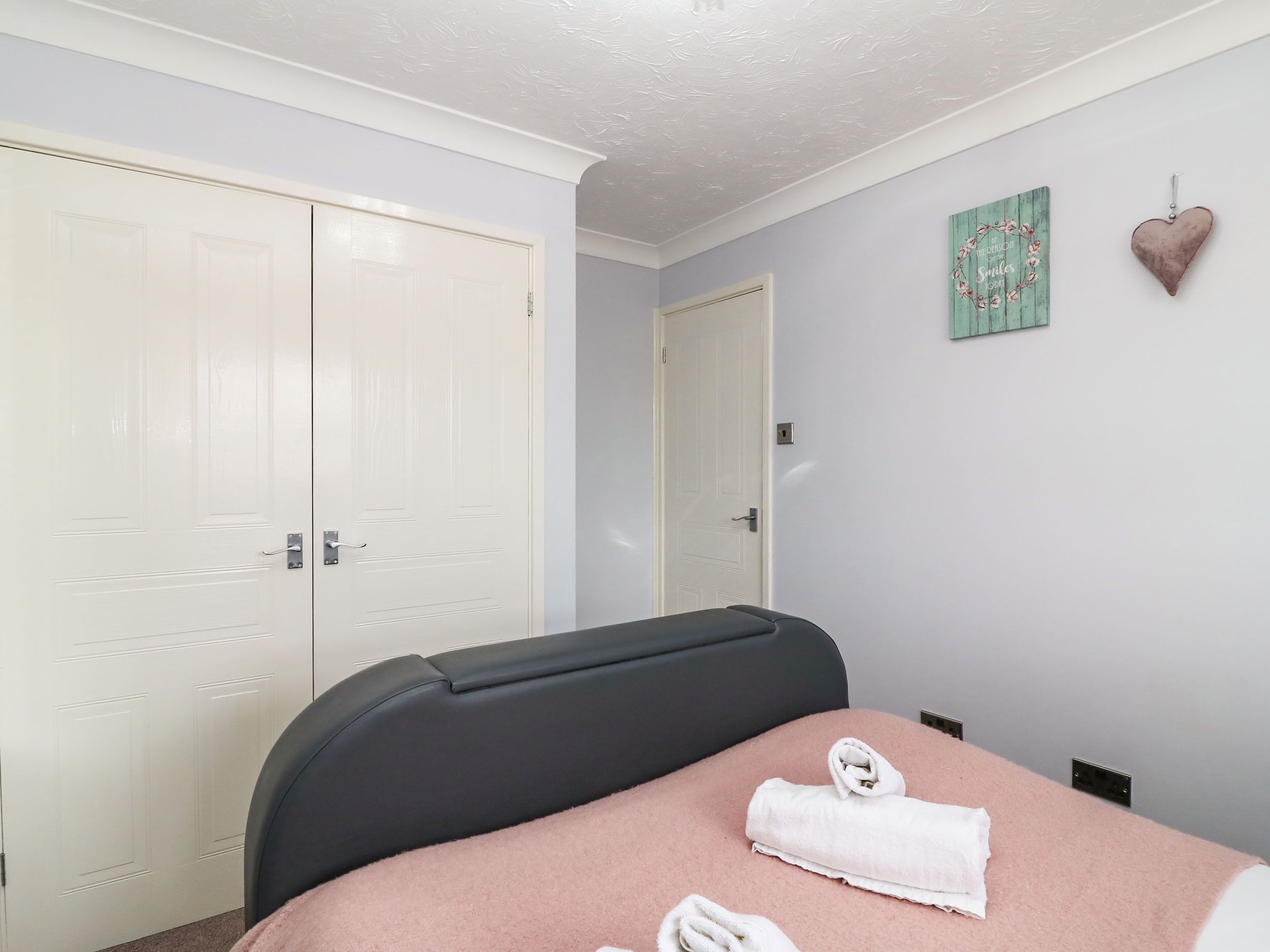 A bedroom with a bed, a white door, a mirror, and a wall decoration.