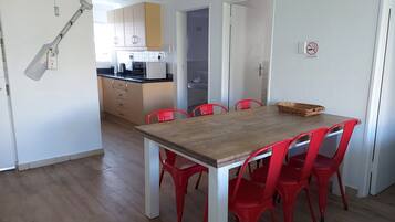 Un comedor con mesa de madera y sillas rojas, una cocina al fondo y un cartel de prohibido fumar en la pared.