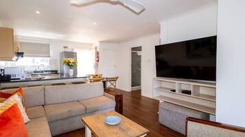 A modern living room with a flat-screen TV, grey sofas, a wooden coffee table, and a ceiling fan.