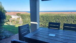 A patio with a table and chairs overlooking a vineyard and distant hills. - First Group Hermanus Beach Club (Hermanus)