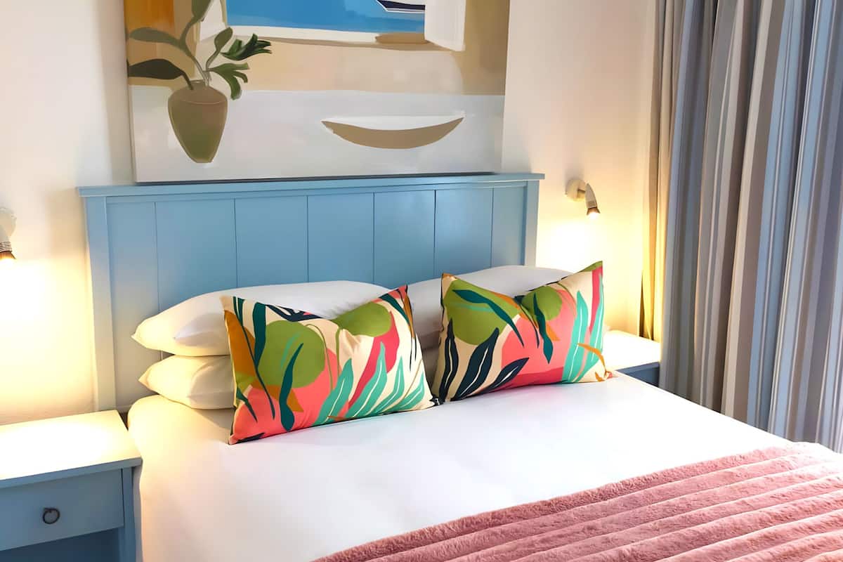 Una cama con cabecera azul, ropa de cama blanca y almohadas coloridas.