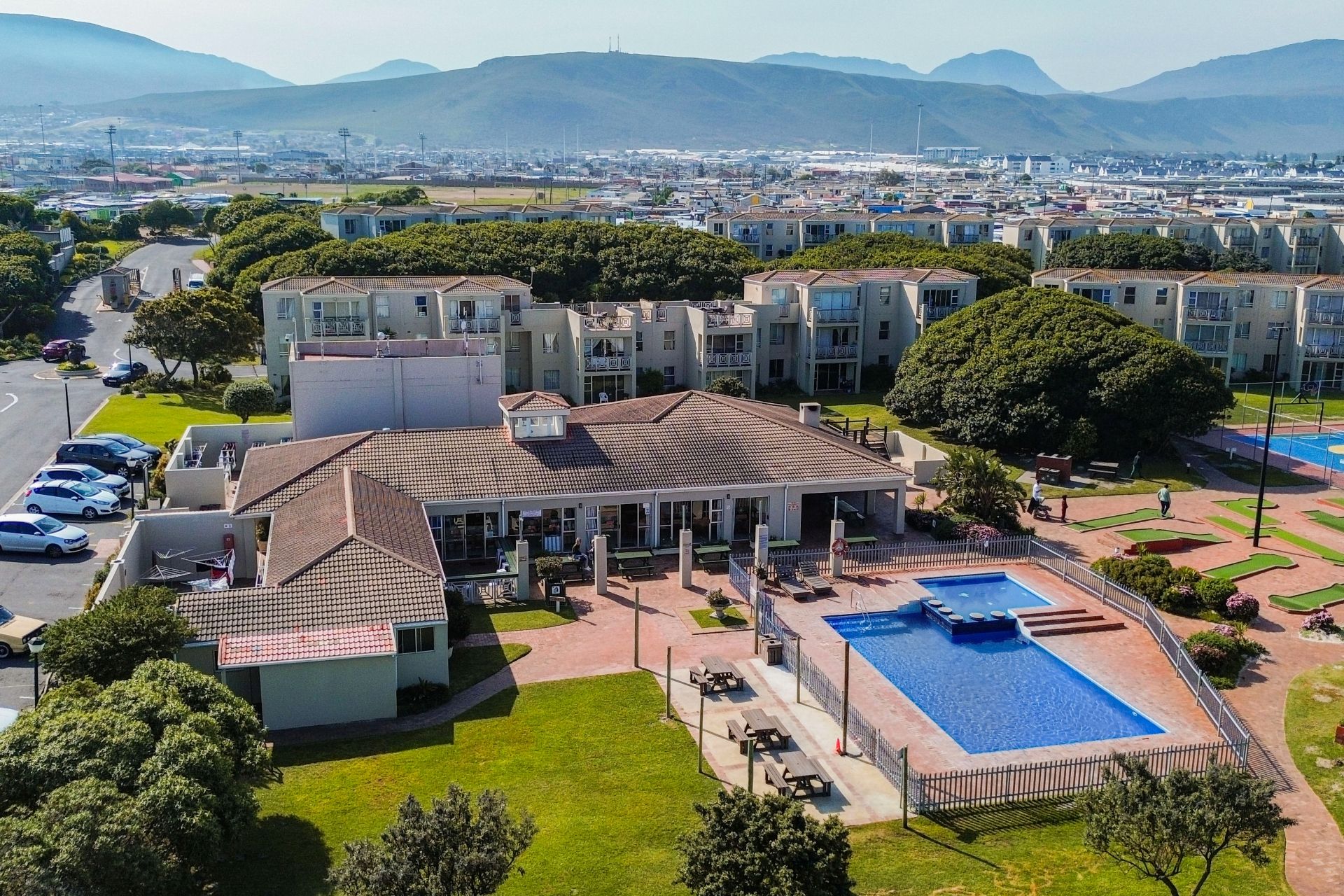 Un quartier résidentiel composé d’immeubles d’appartements, d’une piscine et d’une rue bordée de voitures garées.