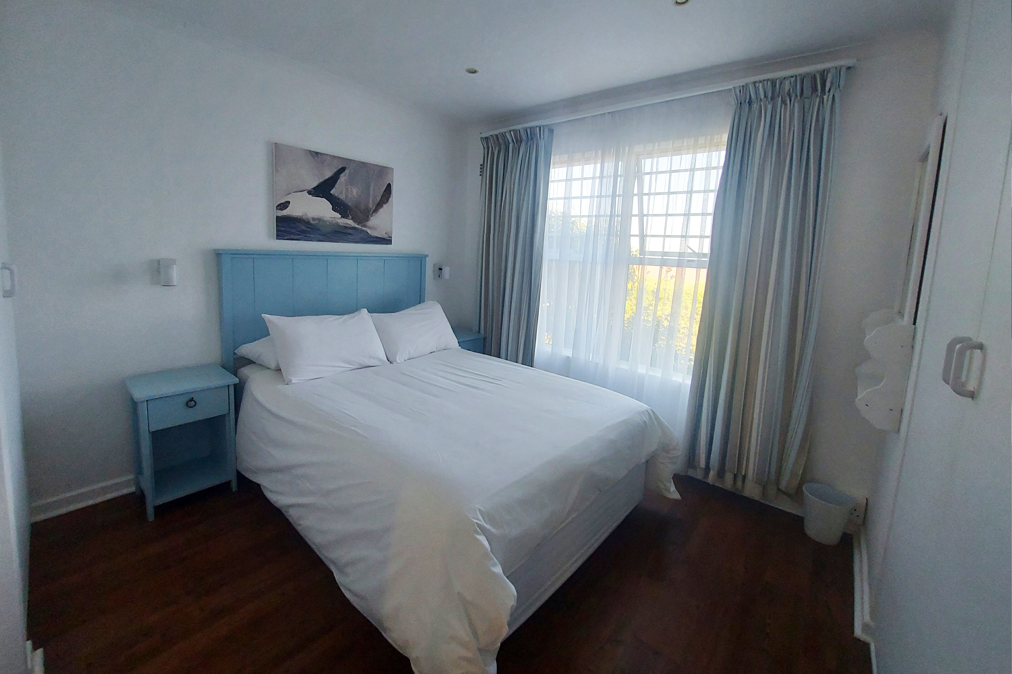 A bedroom with a bed, a nightstand, a window with curtains, and a painting on the wall.