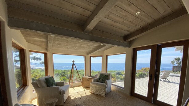 A spacious room with large windows offering ocean views, a wooden ceiling, and a cozy seating area with a small table and cushions.