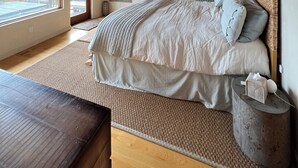 A bedroom with a wooden ceiling, a large bed with a grey and white duvet, a bedside table with a tissue box, and a wall with framed pictures.