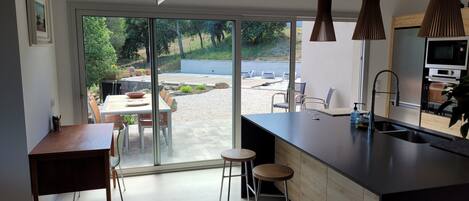 A modern kitchen with a large island, a dining area with a table and chairs, and a sliding glass door leading to an outdoor patio.