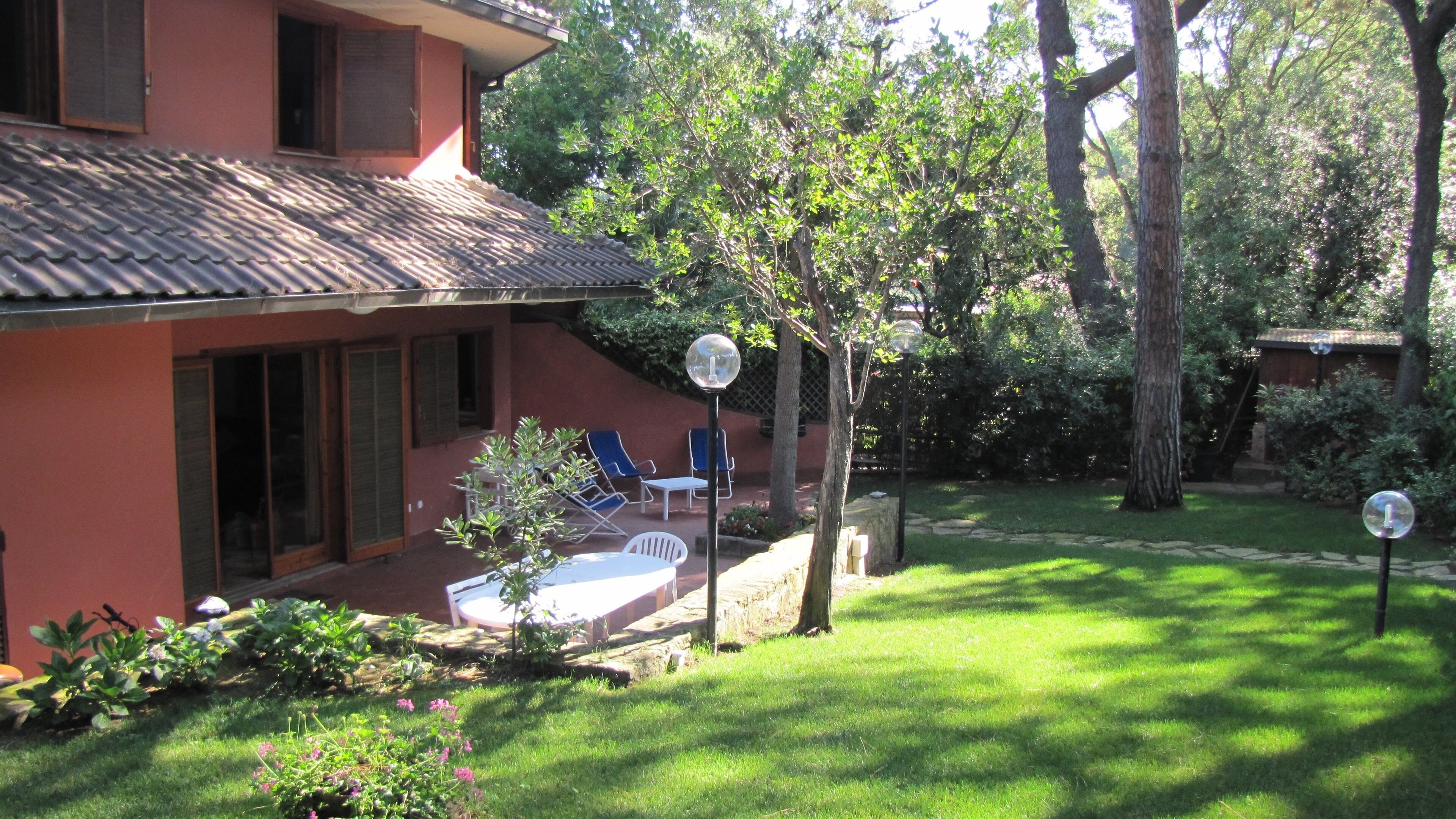 A house with a red exterior, a tiled roof, and a garden with a lawn, a tree, and outdoor furniture.